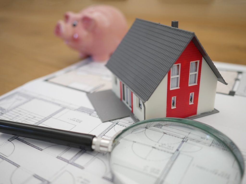 Maqueta de una casa con lupa y planos para analizar el precio real de mercado antes de vender